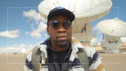 A man in sunglasses is standing in front of a satellite dish.