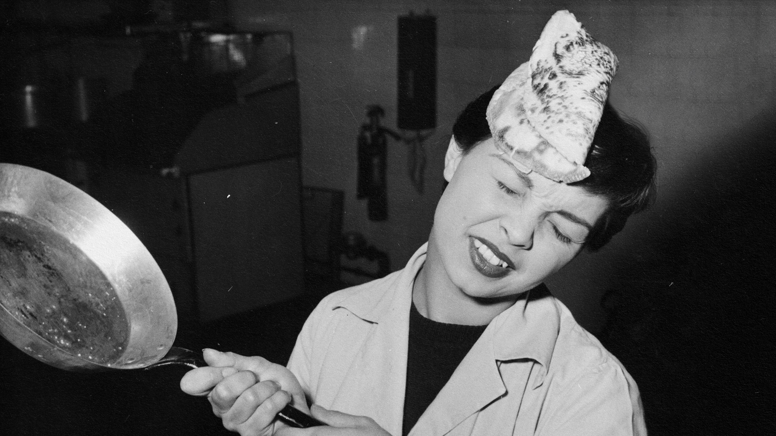 A woman holding a frying pan with an intelligently failed pizza on it.