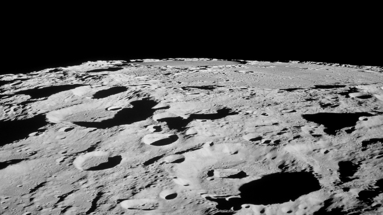 Black and white image of the moon's surface covered with numerous craters of varying sizes under a stark black sky.